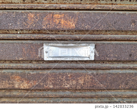 Silver metal handle plate secured on decaying rusted steel shutter surface showcasing industrial architectural details and textures. Silver metal handle plate secured on decaying rusted steel shutter surface showcasing industrial architectural details and textures. 142833236