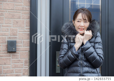 玄関ドアを開けて寒そうな女性 142833755