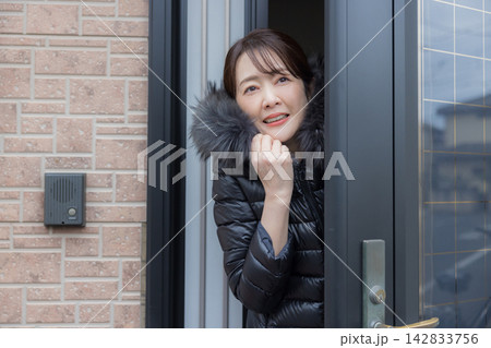玄関ドアを開けて寒そうな女性 142833756