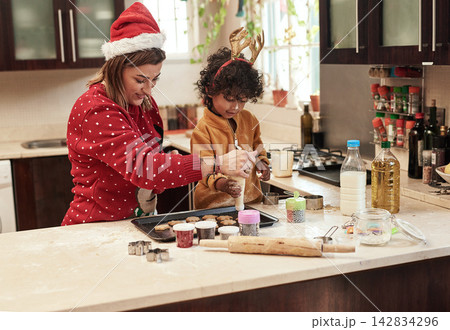 Mother, child and baking with christmas, snack and dough learning for cookies in kitchen together. Smile, food and celebration with woman, adopted son and boy in home to prepare sweet treat or love 142834296