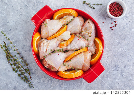Raw Chicken Drumsticks with Oranges and Thyme, prepared for baking in red round baking dish Raw Chicken Drumsticks with Oranges and Thyme, prepared for baking in red round baking dish 142835304
