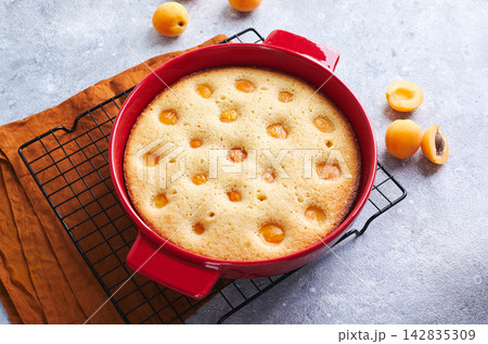 Delicious homemade apricot pie with fresh apricots in red baking dish on gray background. Summer fruit pie. Delicious homemade apricot pie with fresh apricots in red baking dish on gray background. Summer fruit pie. 142835309