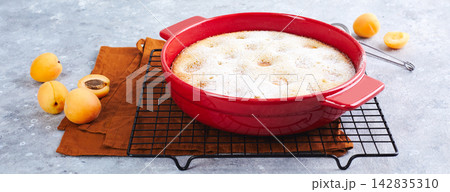 Delicious homemade apricot pie with fresh apricots in red baking dish on gray background. Summer fruit pie. Delicious homemade apricot pie with fresh apricots in red baking dish on gray background. Summer fruit pie. 142835310