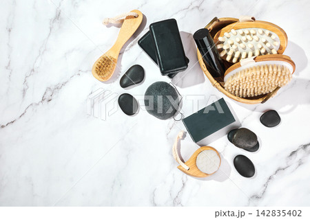 Three pieces of black charcoal soap, Konjac sponge, beauty care products, candles and brushes for washing and massage on marble background 142835402