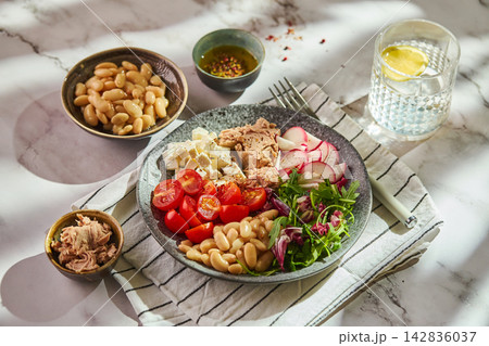 Healthy tuna salad bowl with white beans, feta cheese, tomatoes, radish, and greens on marble table 142836037