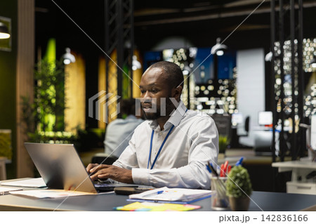Worker typing on laptop keyboard at office desk, doing computer tasks, working overnight. African american man using notebook at work, researching key data for company project Worker typing on laptop keyboard at office desk, doing computer tasks, working overnight. African american man using notebook at work, researching key data for company project 142836166