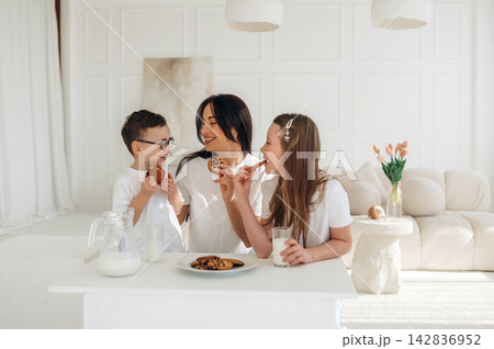 Family enjoying cookies and milk together at a bright kitchen table with a plate of cookies and a glass of milk in a modern, minimalist interior setting 142836952