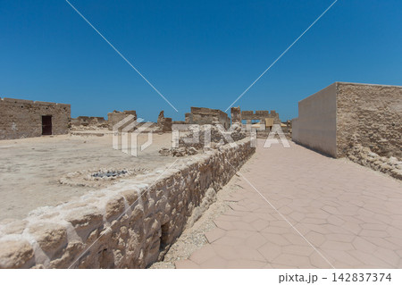 Ruins of an ancient structure in a dry landscape under a clear blue sky during midday 142837374