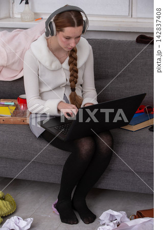 Young woman works on laptop while sitting on gray couch in a cozy living space during the day 142837408
