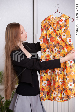 Woman holding a bright dress in a room with plants and light colors during the day Woman holding a bright dress in a room with plants and light colors during the day 142837411