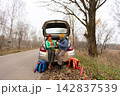 In autumn, an elderly couple enjoys relaxing with warm drinks near a quiet road surrounded by trees and fallen leaves 142837539