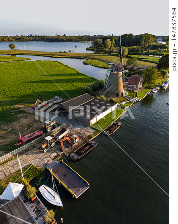 High angle vertical aerial drone photograph of De Faljeril windmill, yard, tractors, work barges, sailboat, polder fields, and Kagerplassen lake in Warmond, South Holland, Netherlands at sunset High angle vertical aerial drone photograph of De Faljeril windmill, yard, tractors, work barges, sailboat, polder fields, and Kagerplassen lake in Warmond, South Holland, Netherlands at sunset 142837564