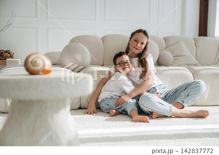 Mother and son sitting together on a light-colored sofa in a modern living room, with a decorative shell on a stone table in the foreground 142837772