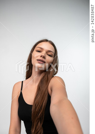 Young woman taking a selfie, capturing a vertical portrait with long brown hair, wearing a black camisole Young woman taking a selfie, capturing a vertical portrait with long brown hair, wearing a black camisole 142838487