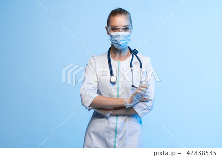 Healthcare professional in mask, goggles, and stethoscope holding syringe, symbolizing vaccination and medicine Healthcare professional in mask, goggles, and stethoscope holding syringe, symbolizing vaccination and medicine 142838535