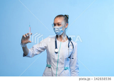 Healthcare professional holding syringe with vaccine, preparing for injection, medical worker wearing mask and goggles Healthcare professional holding syringe with vaccine, preparing for injection, medical worker wearing mask and goggles 142838536