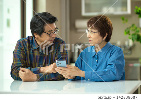 リビングで一緒にスマホを見るシニアの夫婦 リビングで一緒にスマホを見るシニアの夫婦 142838687
