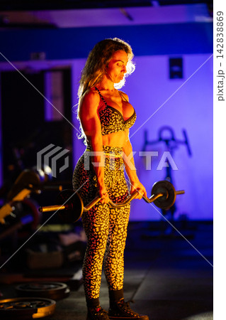 Strong person lifts weights in a gym with bright lighting and dark background during evening workout session Strong person lifts weights in a gym with bright lighting and dark background during evening workout session 142838869