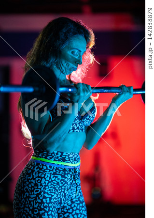 Person lifts weights in a gym with colorful lights during evening workout session Person lifts weights in a gym with colorful lights during evening workout session 142838879