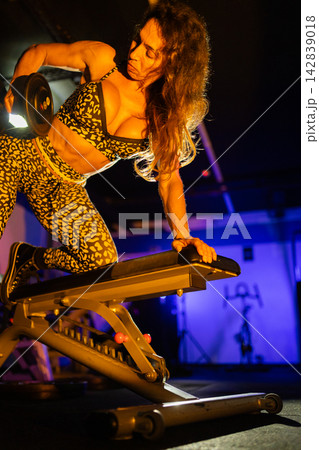 Woman lifts dumbbell during workout in gym with blue lighting and focus on fitness and strength training Woman lifts dumbbell during workout in gym with blue lighting and focus on fitness and strength training 142839018