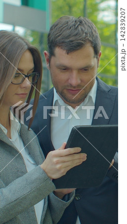 Vertical video. Business people standing near business center with digital tablet. Man and woman read news on Tablet Computer near office in morning. Vertical video. Business people standing near business center with digital tablet. Man and woman read news on Tablet Computer near office in morning. 142839207