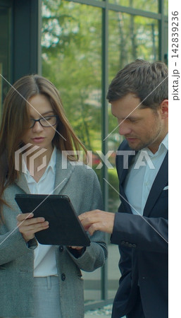 Vertical video. Business people going to work with digital tablet on street. Man and woman walking near office in morning. Vertical video. Business people going to work with digital tablet on street. Man and woman walking near office in morning. 142839236