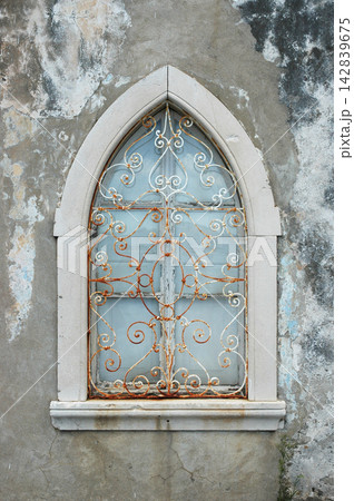Gothic pointed window with ornate rusty security grill Gothic pointed window with ornate rusty security grill 142839675