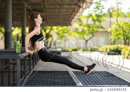 Fit young woman doing back push ups and looking focused and involved 142840145