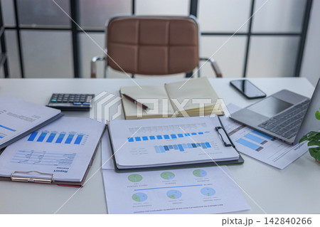 Modern white office workspace of financial or accounting tasks, featuring a laptop, a tablet, financial charts, reports, a calculator, and a notebook on a white desk. Modern white office workspace of financial or accounting tasks, featuring a laptop, a tablet, financial charts, reports, a calculator, and a notebook on a white desk. 142840266