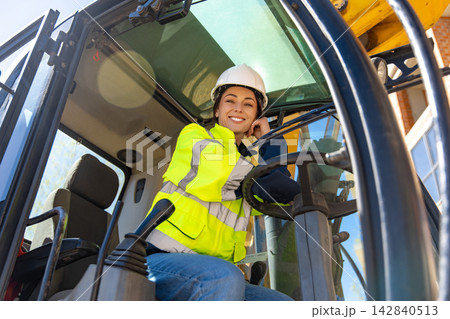 Happy female heavy equipment operator smiling inside excavator cabin 142840513