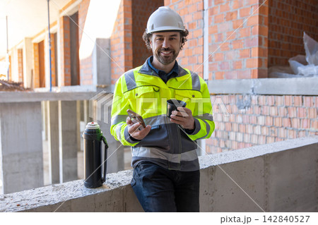 Cheerful construction manager holding smartphone and cup 142840527