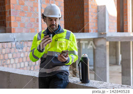 Male architect drinking hot beverage and using smartphone Male architect drinking hot beverage and using smartphone 142840528
