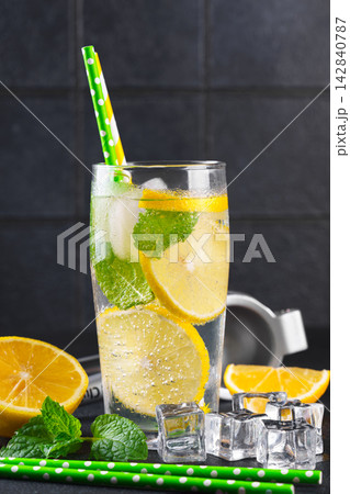 Fresh homemade lemonade with lemon slices, mint and ice in glasses on black kitchen tile background Fresh homemade lemonade with lemon slices, mint and ice in glasses on black kitchen tile background 142840787