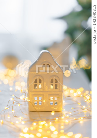 Minimalist Christmas decor, ceramic house on garland warm festive fairy lights background 142840815