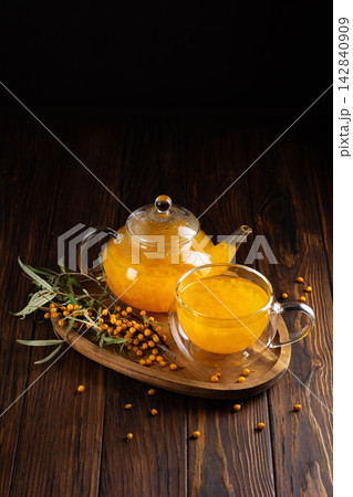 Warm sea buckthorn tea in glass teapot and cup with fresh berries on wooden background Warm sea buckthorn tea in glass teapot and cup with fresh berries on wooden background 142840909