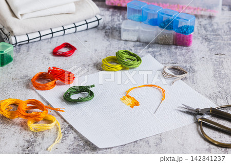 Cross-stitch, Aida cloth, colorful embroidery floss, and scissors on the table. 142841237