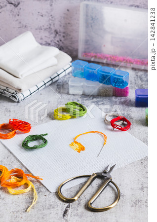 Cross-stitch, Aida cloth, colorful embroidery floss, and scissors on the table vertical view Cross-stitch, Aida cloth, colorful embroidery floss, and scissors on the table vertical view 142841238