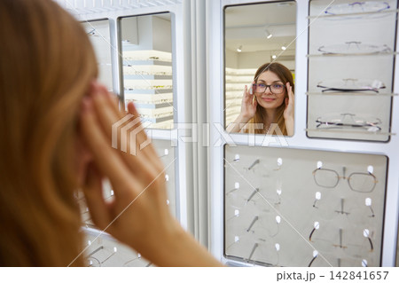 Woman customer smiles while fitting new eyeglasses in boutique Woman customer smiles while fitting new eyeglasses in boutique 142841657