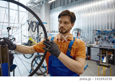 Professional worker adjusting bike wheel in busy workshop setting Professional worker adjusting bike wheel in busy workshop setting 142842036
