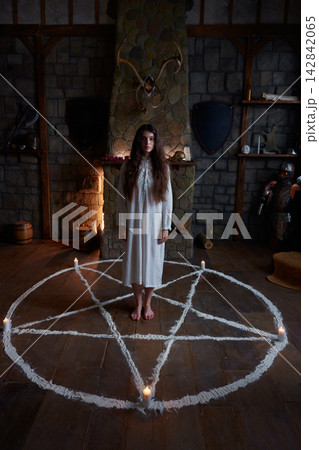 Caucasian woman standing inside exorcism pentagram circle, candlelit medieval chamber 142842065