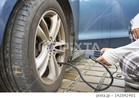Person inflating car tire with portable air compressor beside vehicle. Concept of car maintenance 142842401