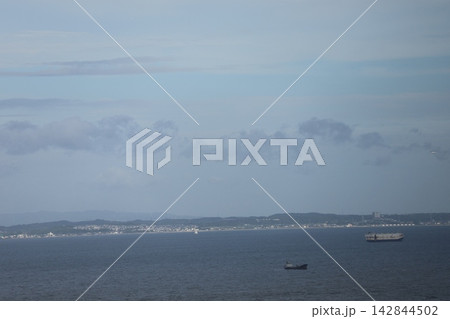 青い海面の海と船と海岸沿いの町並みと山と霞む山並みと雲と青空の風景 青い海面の海と船と海岸沿いの町並みと山と霞む山並みと雲と青空の風景 142844502