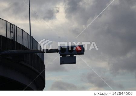 雲の多い青空と高速道路橋と赤く点灯する信号機のアップの風景 142844506