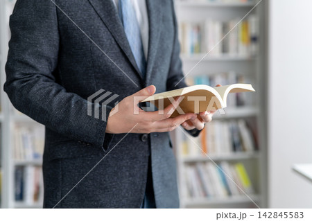 書斎で本を手に取り読書するスーツ姿のビジネスマン 書斎で本を手に取り読書するスーツ姿のビジネスマン 142845583