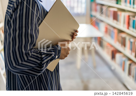 図書館でノートパソコンを抱えて歩くストライプシャツの女性 図書館でノートパソコンを抱えて歩くストライプシャツの女性 142845619