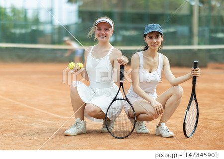 Two young women in sportswear against backdrop of outdoor tennis court 142845901