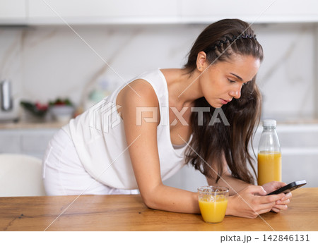 Young woman drinking juice and scrolling through social media on mobile Young woman drinking juice and scrolling through social media on mobile 142846131
