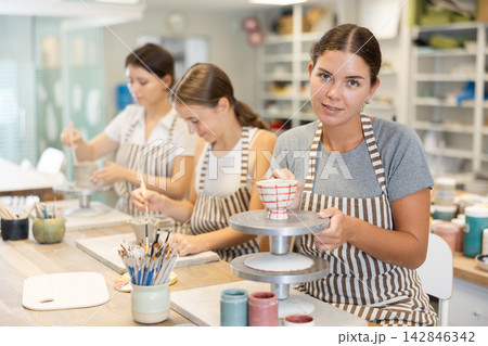 Young woman painting ceramic cup in workshop Young woman painting ceramic cup in workshop 142846342