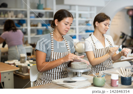 Girls perform work on molding blanks from raw clay and painting staining them Girls perform work on molding blanks from raw clay and painting staining them 142846354