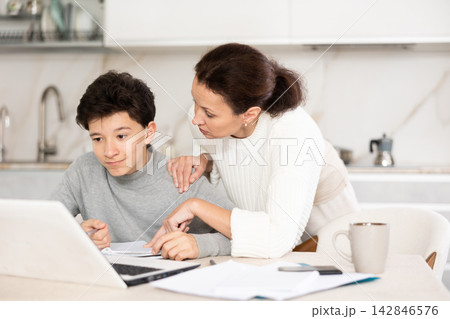 Boy does school homework with his mother and solves mathematical problems in kitchen Boy does school homework with his mother and solves mathematical problems in kitchen 142846576